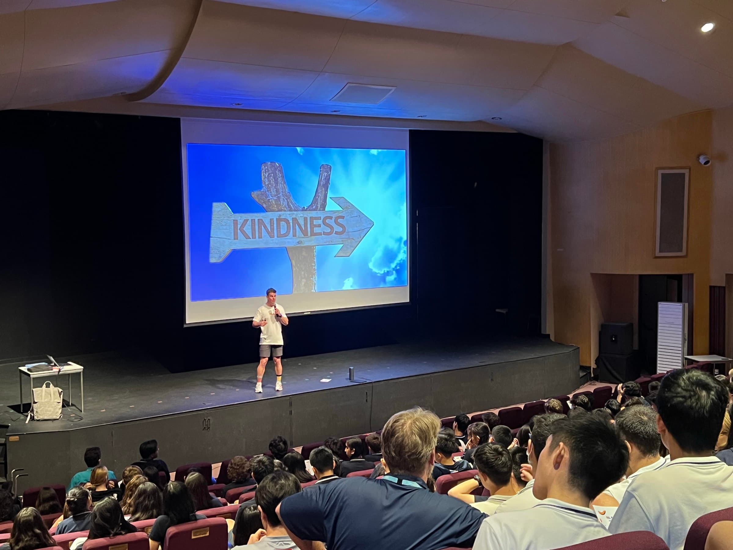Dale Sidebottom on stage in a full auditorium, presenting to a seated audience