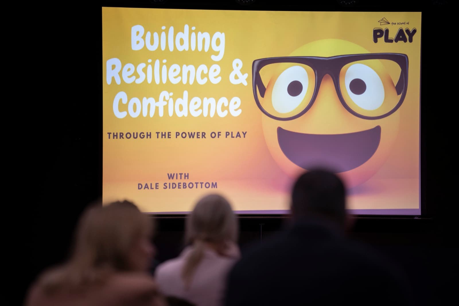 An audience in silhouette facing a screen that reads Building Resilience and Confidence through the power of play