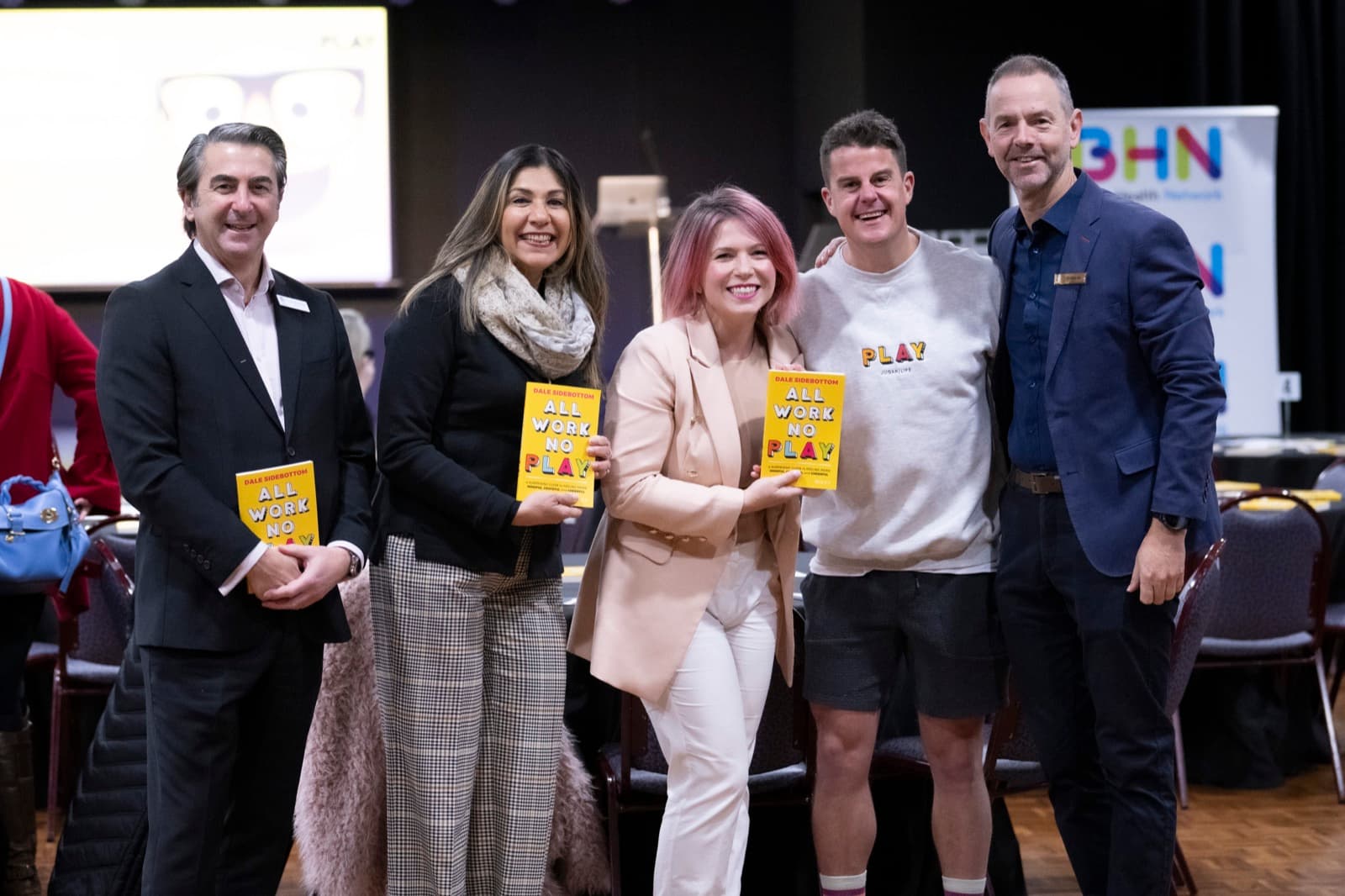 A group of five people standing together at a workshop, three of them holding copies of a book