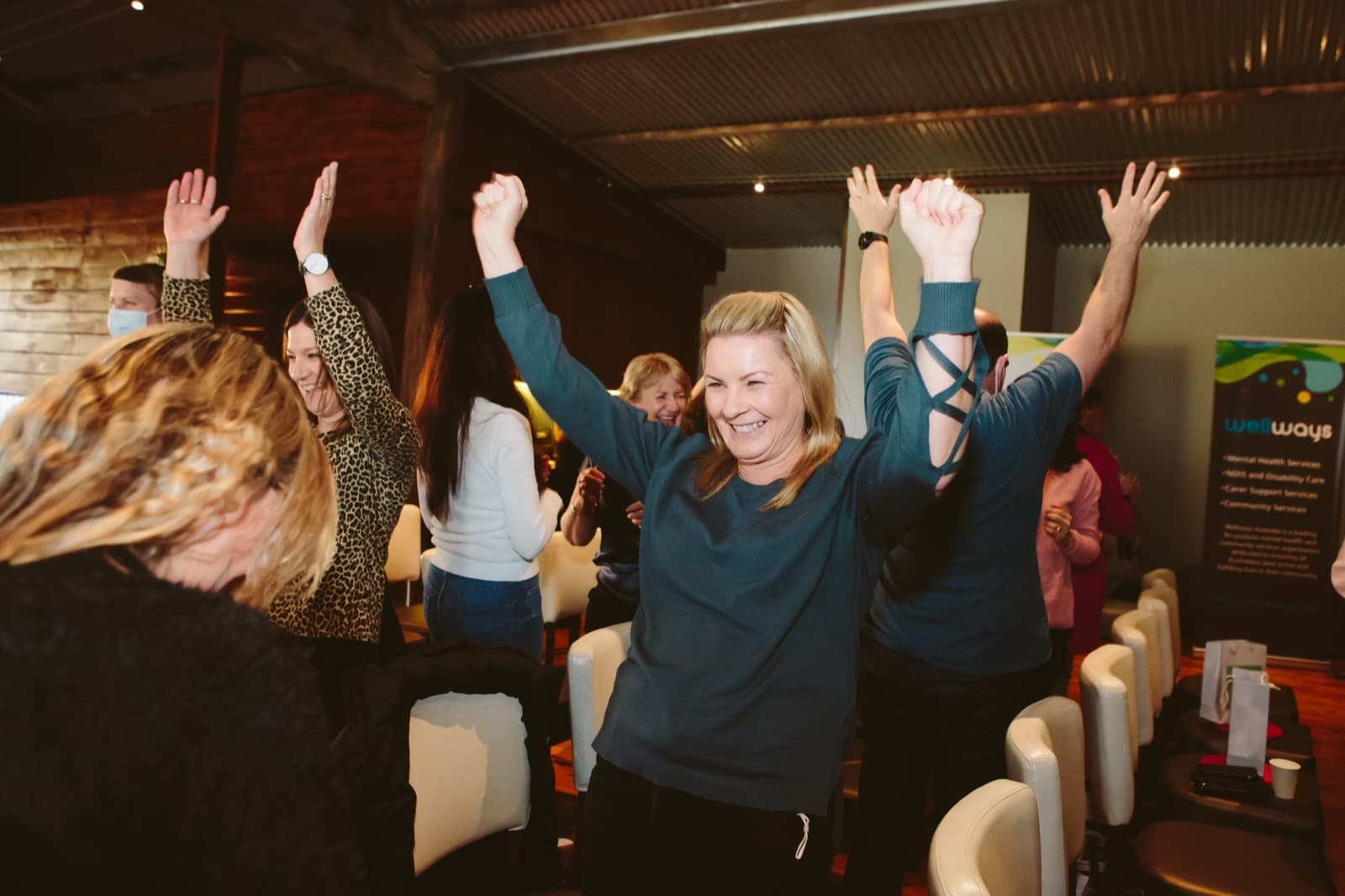 Participants standing with their hands in the air, laughing, during a live Better Us Project facilitated session
