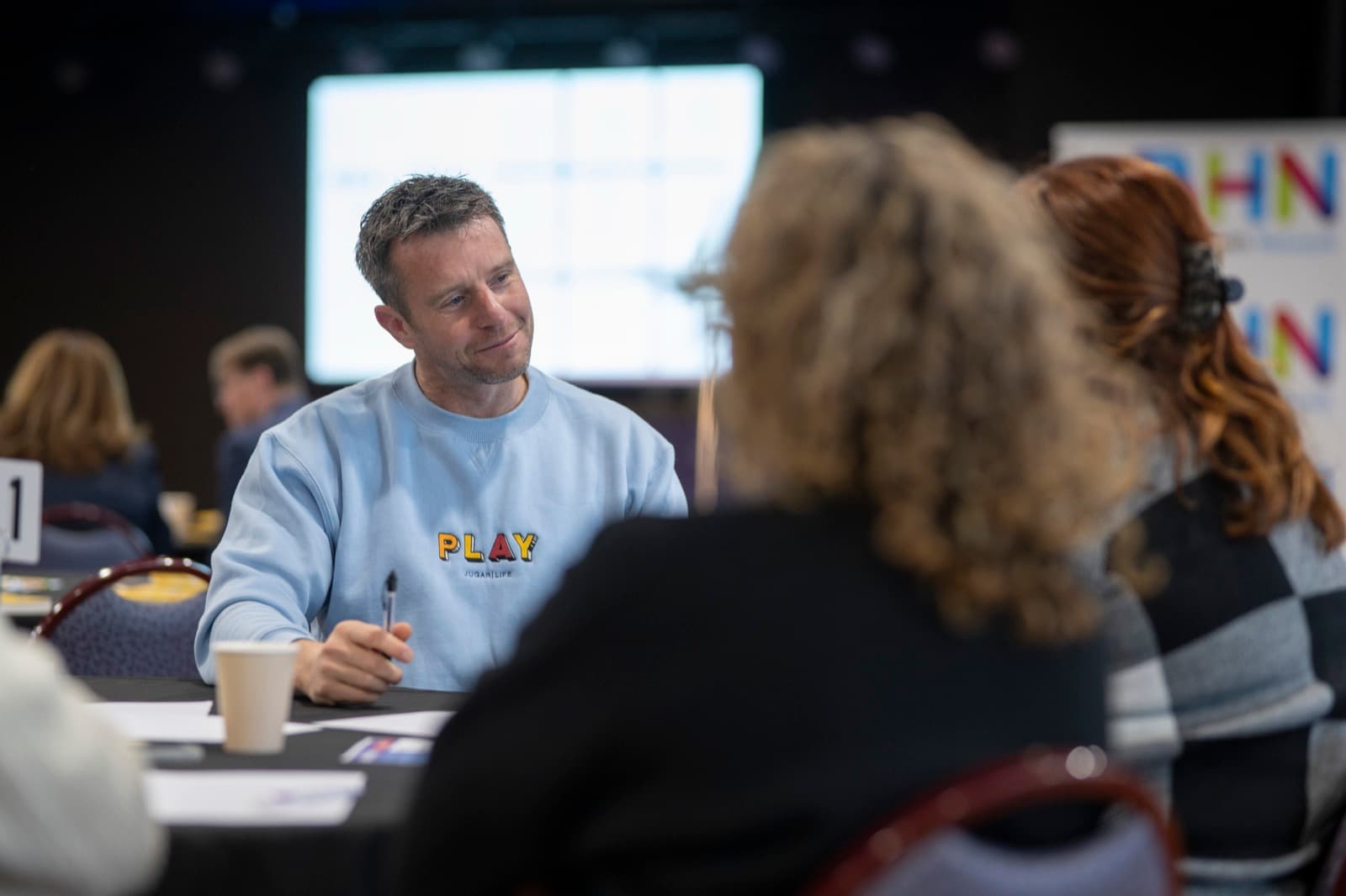 A Better Us Project facilitator sitting at a table, listening to participants during a live session