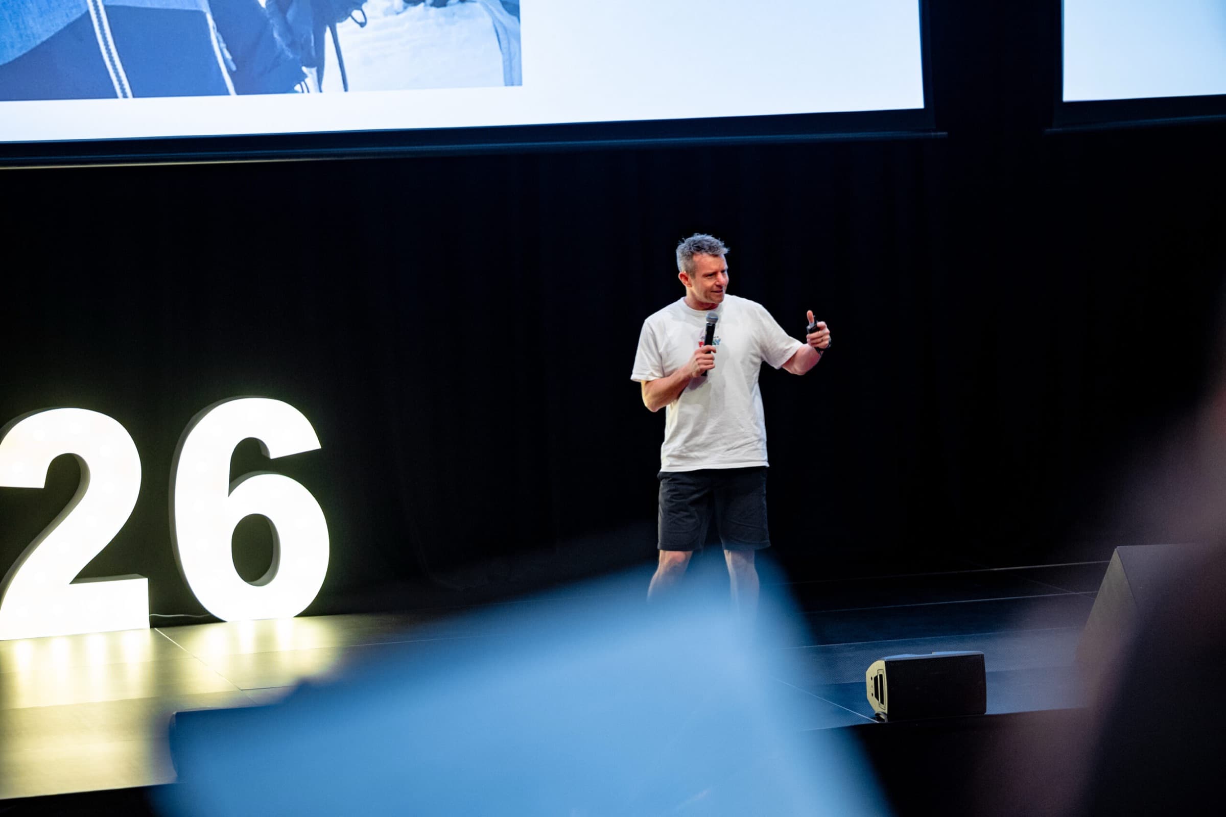 A Better Us Project facilitator alone on a darkened stage with a microphone, beside large illuminated numerals