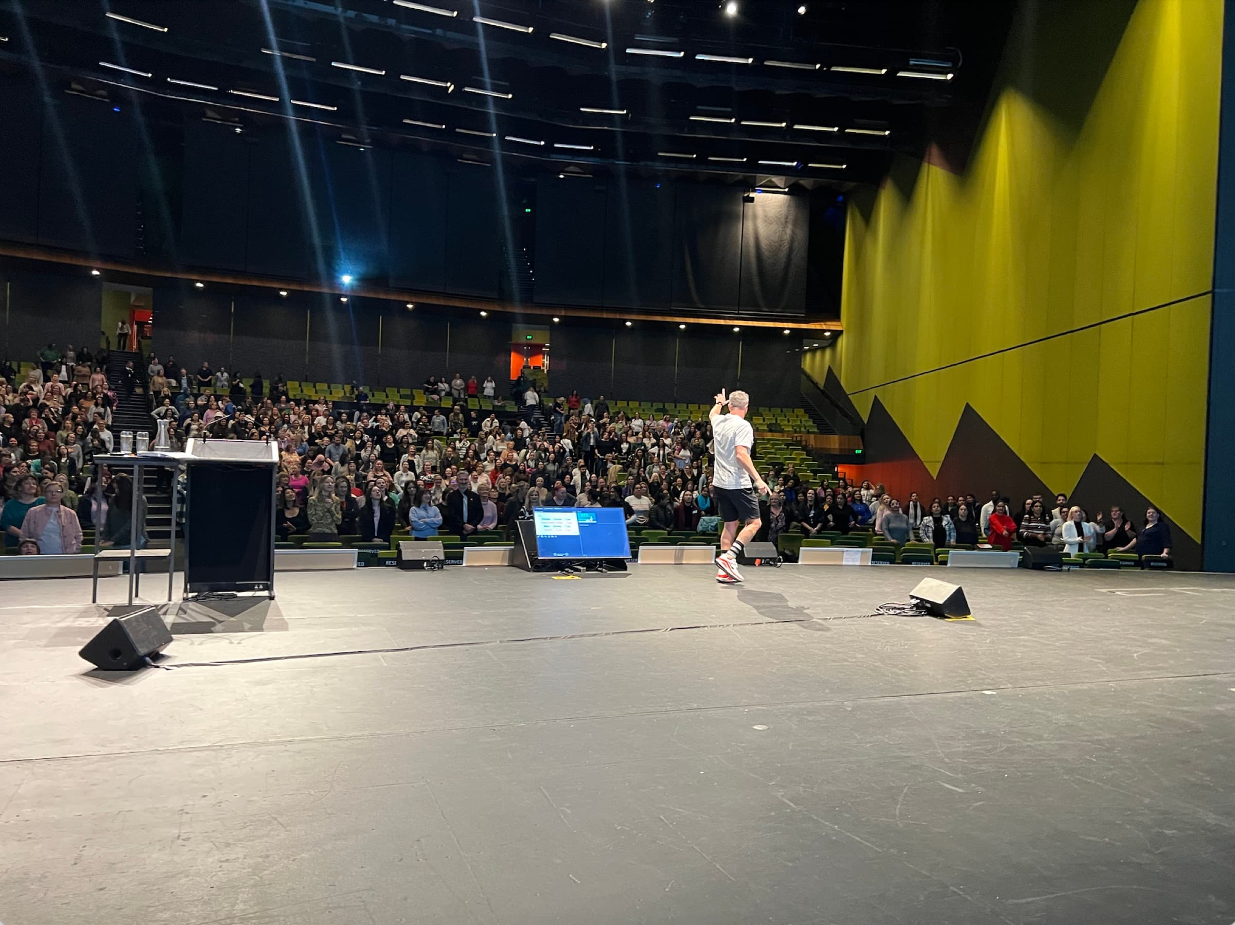 A Better Us Project facilitator alone on a large theatre stage, facing a full and steeply banked audience
